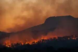 Wildfire burning along a California ridgeline at dusk above open grazing land